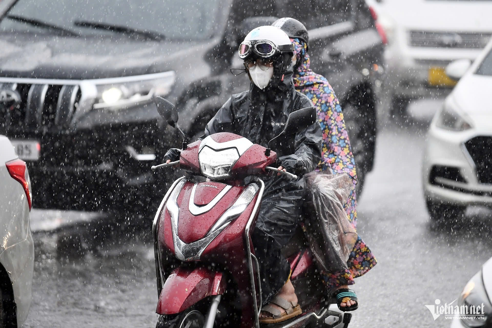 Người đi xe máy đội mưa lớn trên đường Hà Nội, đèn pha bật sáng giữa dòng ô tô