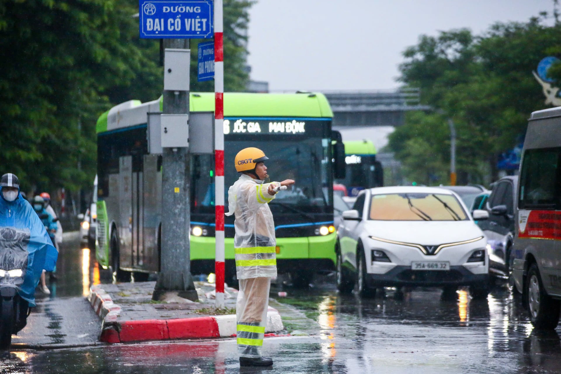 CSGT phân luồng dưới trời mưa, mặt đường ướt phản chiếu ánh đèn xe