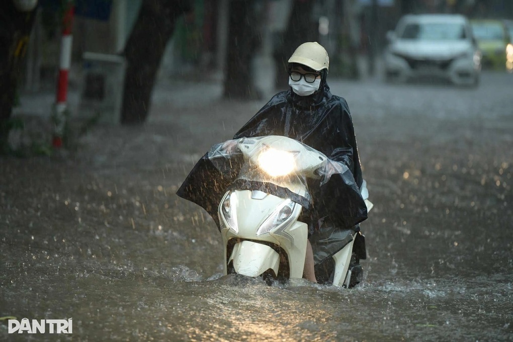 Người đi xe máy lội qua vùng nước ngập trong mưa, đèn pha bật gần sát mặt nước